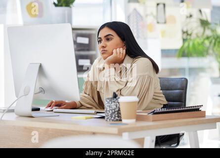 Eine gelangweilte, faule und müde Mitarbeiterin, die im Büro an einem Computer arbeitet und sich auf ihren Schreibtisch lehnt. Eine überarbeitete Geschäftsfrau ist verärgert und frustriert, weil sie an ihrem Tisch sitzt und sich ausgebrannt fühlt Stockfoto