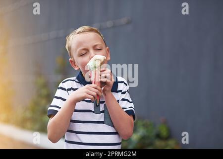 Dieses Eis ist wirklich gut. Ein kleiner Junge genießt einen Eiskegel. Stockfoto