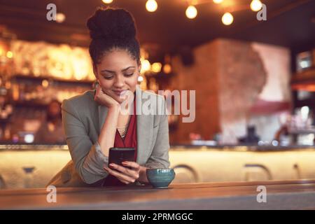 Sie verbringt gerne Zeit in ihrem lokalen Café. Eine junge Geschäftsfrau schreibt in einem Café auf einem Handy. Stockfoto