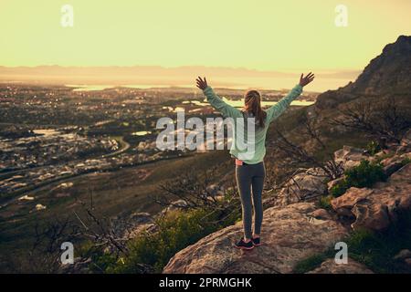 Sie hat es geschafft. Rückansicht einer sportlichen jungen Frau, die mit ausgestreckten Armen im Freien steht. Stockfoto