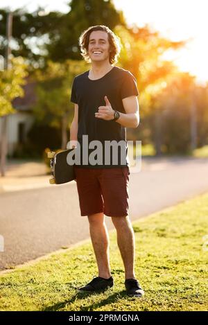 Lasst uns skaten, bis die Sonne untergeht. Porträt eines jungen Mannes, der mit seinem Skateboard draußen steht. Stockfoto