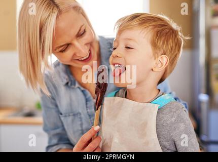 Das Beste am Backen ist, den Löffel zu lecken. Eine Mutter gibt ihrem Sohn einen Löffel Schokoladenteig zum Ablecken. Stockfoto