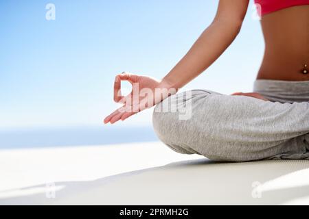 Eine junge Frau meditiert während sie an einem sonnigen Tag im Freien Yoga macht. Stockfoto