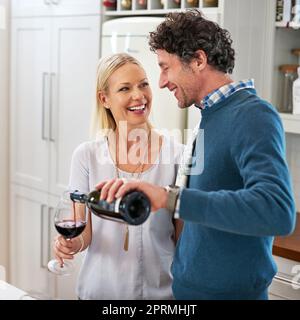 Ein glückliches Paar, das zusammen in ihrer Küche zu Hause Wein trinkt. Stockfoto