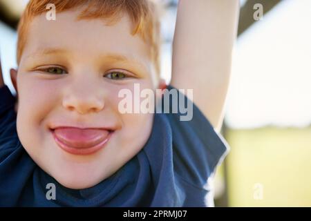 Neener Neener. Porträt eines Jungen, der aus seiner Zunge ragt, während er an einer Dschungelturnhalle hängt. Stockfoto