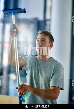 Ein junger Mann, der die Fenster im Büro putzte. Stockfoto