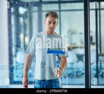 Er ist stolz auf seine Reinigung. Ein junger Mann putzt die Fenster im Büro. Stockfoto
