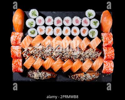 Maki und Brötchen mit Thunfisch, Lachs, Garnelen, Krabben und Avocado werden auf Steinschiefer serviert. Stockfoto