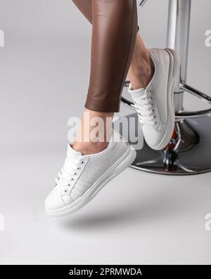 Stylische, moderne Damenschuhe auf den Beinen des Models, die im Studio auf einem Stuhl sitzen und einen weißen Hintergrund haben. Stockfoto