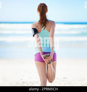 Streckt ihre Muskeln. Rückansicht einer jungen Frau, die sich vor einem Work-out am Strand ausdehnt. Stockfoto