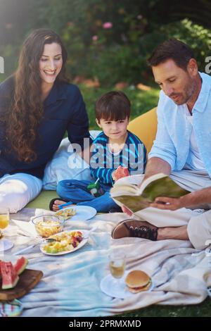 Kostbare Momente im Park. Eltern lesen ihrem Sohn während eines Picknicks im Park ein Buch vor. Stockfoto