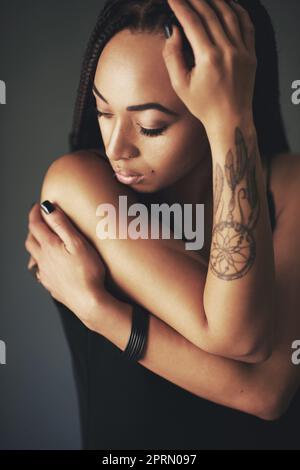 Sie trägt ihre Emotionen auf ihrem Ärmel. Studioaufnahme einer schönen jungen Frau mit einem Tattoo auf ihrem Arm vor einem grauen Hintergrund. Stockfoto