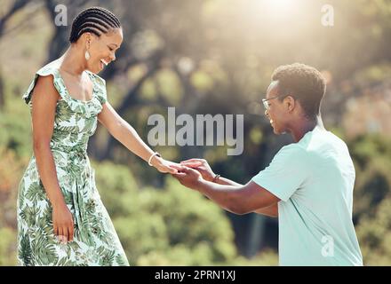 Liebe, Verlobung und schwarzer Mann machen ihrer Freundin einen Heiratsantrag, bei einem romantischen Date draußen, glücklich und aufgeregt. Eine afrikanische Frau überrascht mit einer süßen Geste und genießt einen besonderen Beziehungsmoment bei einem gemeinsamen Date im Freien Stockfoto