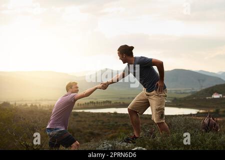 Du wirst auf dem Weg keine helfende Hand finden. Ein freundlicher junger Wanderer, der seinem Freund hilft, auf einen Felsen auf einem Bergpfad zu klettern Stockfoto