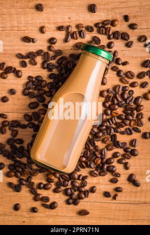 Kaffeemilch in Glasflasche und Kaffeebohnen auf dem Holztisch. Stockfoto