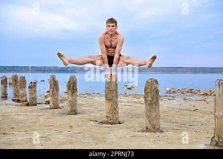 Der Muscular man Yogi stellt sich auf Holzsäulen auf seine Hände. Stockfoto