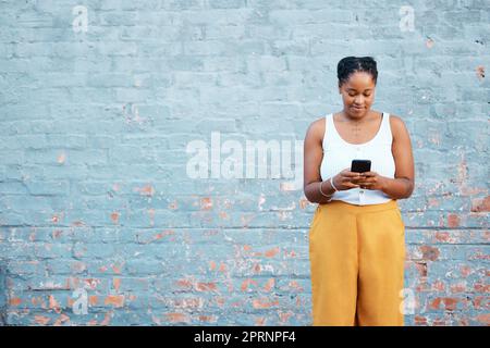 Schwarze Frau, Mode und Telefon an der Mauer in Nigerian für Marketing, Werbung oder Verkaufsförderung. Lächeln, glücklich oder trendig Stockfoto