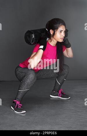 Spüren Sie das Brennen. Studioaufnahme einer attraktiven jungen Frau, die mit Hanteln vor grauem Hintergrund arbeitet. Stockfoto