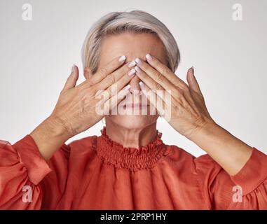 Senioren, Hände und Augen oder Gesicht von reifer Frau, die unter Kopfschmerzen oder Augenbelastung leidet, während sie vor einem grauen Studiohintergrund posiert. Ältere Frau mit Sehstörungen. Stockfoto