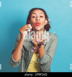 Mögen alle Ihre Probleme Blasen sein. Porträt einer jungen Frau, die vor blauem Hintergrund Blasen bläst. Stockfoto