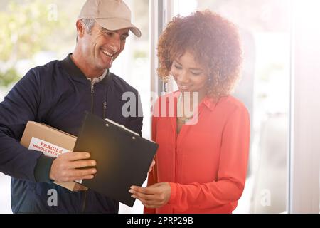 Ein Kurier, der eine Lieferung an einen lächelnden Kunden macht. Stockfoto