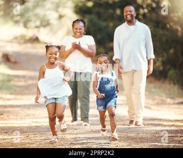 Glückliche, schwarze Familie und Kinder laufen im Sommer im Naturpark, während mom und Dad ihre kleinen afrikanischen Kinder anfeuern. Spielen, Lifestyle und aktive Eltern, die mit ihren gesunden Mädchen in einem Wald wandern Stockfoto