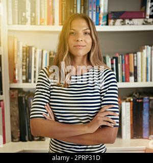 Genießen Sie die Freiheit des Freiberufens. Porträt einer Frau, die in ihrem Heimbüro vor Bücherregalen steht. Stockfoto