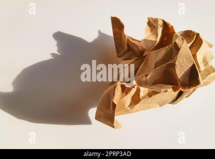 Eine zerknitterte Papierkugel aus braunem Kraftpapier mit Schatten auf hellem Hintergrund, Draufsicht Stockfoto