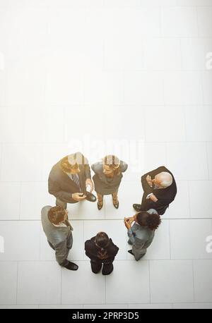 Reden wir über Geschäfte. Eine Aufnahme einer Gruppe von Geschäftsleuten, die sich in der Bürolobby unterhalten. Stockfoto