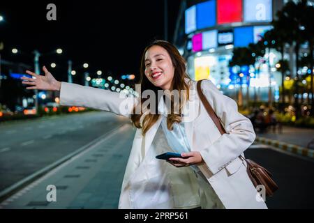 Eine Geschäftsfrau, die in der belebten Straße nachts mit einem Hageltaxi winkt, winkt Stockfoto