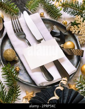 Schwarzer und goldener Weihnachtstisch mit Platzkarte, Ziergegenständen und Tannenästen. Modell Stockfoto