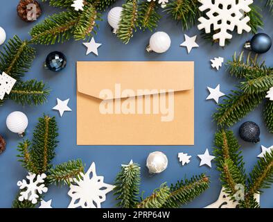 Handgefertigter Papierumschlag auf blauem Hintergrund in der Nähe weißer Weihnachtsdekorationen und Tannenzweige Stockfoto