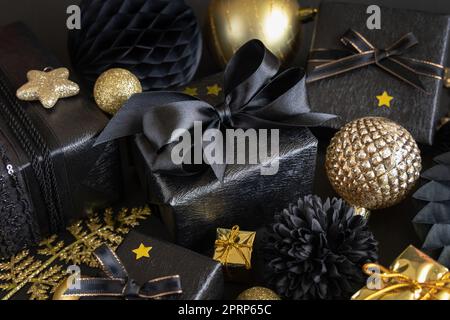 Weihnachtsgeschenkbox mit Schleife in der Nähe von schwarzen und goldenen Ornamenten und Kugeln Stockfoto