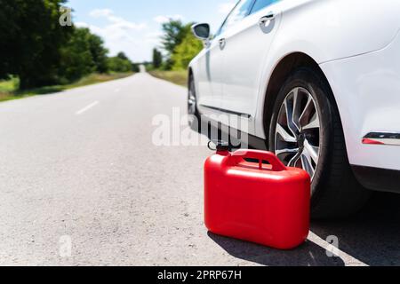 Ein Auto, das am Straßenrand geparkt ist, ein leerer roter Kanister. Der Fahrer ist unterwegs. Hilfe auf der Straße. Kraftstoffmangel - Öl, Diesel, Benzin. Stockfoto