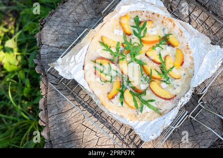 Sehr leckere und interessante Pizza mit Pfirsich und Dor Blue mit Rucola. Köstliche, interessante Fruchtpizza. Gegrillte Pizza, Erholung im Freien. Stockfoto