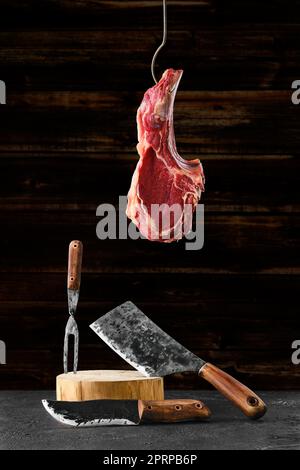 Rind Ribeye Steak Knochen-in auf Stahlhaken über dem geschmiedeten Metzger-Set Stockfoto