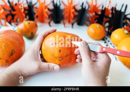 Halloween Oktober 31.. Ein Mann schneidet einem Kürbis mit einem Messer das Gesicht. Blick von oben Stockfoto