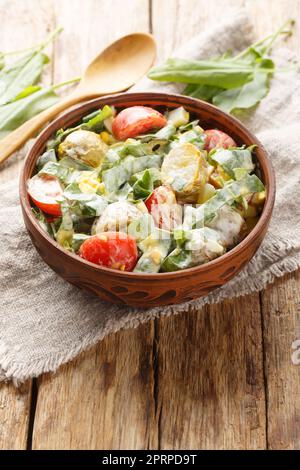 Frischer Salat aus Eiern, Kartoffeln, Tomaten und Sorrel gewürzt mit Sahne-Sauce Nahaufnahme in einer Schüssel auf einem Holztisch. Vertikal Stockfoto