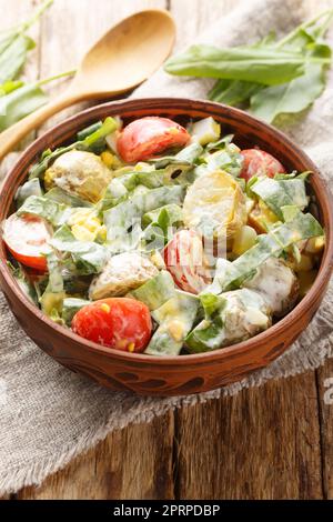 Salat aus gekochten Eiern, Kartoffeln, Tomaten und frischen Kräutern, gewürzt mit Sahne-Sauce, Nahaufnahme in einer Schüssel auf einem Holztisch. Vertikal Stockfoto