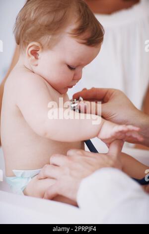 Shes neugierig auf diese Untersuchung. Ein Mädchen, das von einem Arzt untersucht wird, während ihre Mutter im Hintergrund steht. Stockfoto