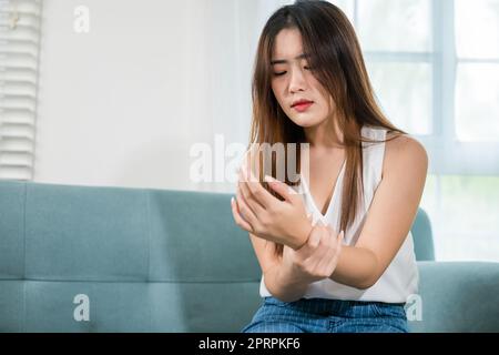 Asiatische junge Frau sitzt auf dem Sofa hält leiden ihr Handgelenk zu Hause Stockfoto