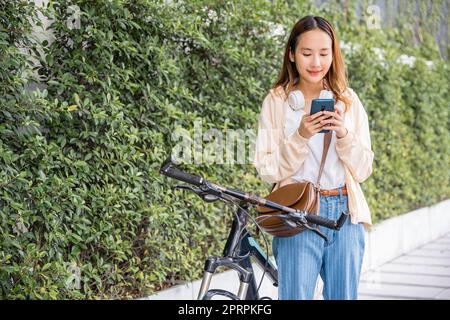 Frau pendelt im Sommer mit dem Fahrrad auf dem Smartphone in Parklandschaft Stockfoto