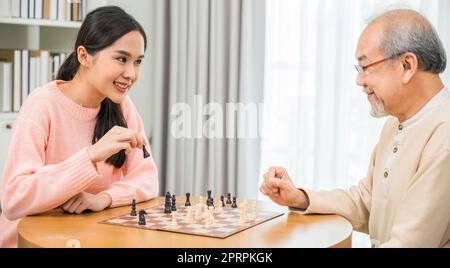 Eine schöne junge lächelnde Frau, die zu Hause mit älteren Menschen Schach spielt Stockfoto