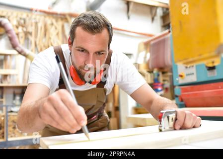 Freundlich Tischler mit Gehörschutz und Arbeitskleidung arbeiten an einer Säge in der Werkstatt Stockfoto