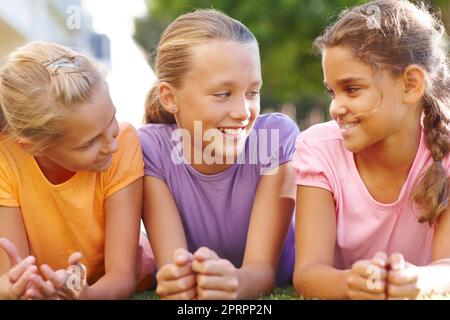 Nachholbedarf nach der Schule. Drei süße Mädchen liegen auf dem Gras und unterhalten sich in der Sonne.