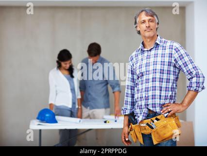 Selbstbewusster Architekt mit Kunden im Hintergrund. Porträt eines selbstbewussten, reifen Architekten mit einem Paar, das den Bauplan im Hintergrund untersucht. Stockfoto