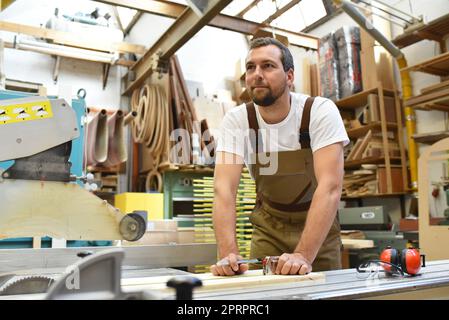 Freundlich Tischler mit Gehörschutz und Arbeitskleidung arbeiten an einer Säge in der Werkstatt Stockfoto