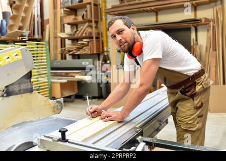 Freundlich Tischler mit Gehörschutz und Arbeitskleidung arbeiten an einer Säge in der Werkstatt Stockfoto