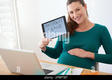 Zeit, sich auf das Baby vorzubereiten. Eine Schwangerin, die eine Tablette mit den Worten Mutterschaftsurlaub auf dem Bildschirm hält. Stockfoto