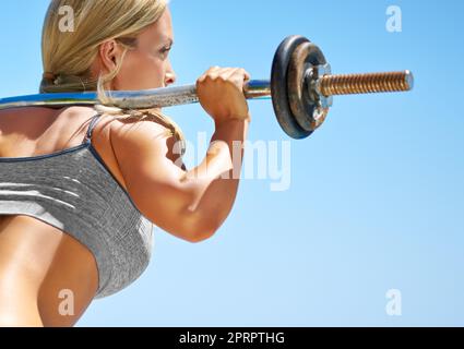 Eine junge Frau hockt mit einer Langhantel draußen. Stockfoto